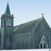 A stone church with a tall spire, arched windows, and a pointed roof under a clear sky.