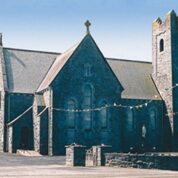 Stone church with tall tower and arched windows, decorated with colourful bunting, against a clear blue sky.
