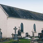 A small white church with arched windows, surrounded by old gravestones in a grassy graveyard.