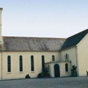 Cream-coloured church with tall, narrow windows and a square bell tower, set against a clear sky.