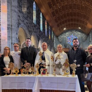 A group of people stand behind a table displaying several golden reliquaries inside a stone church.