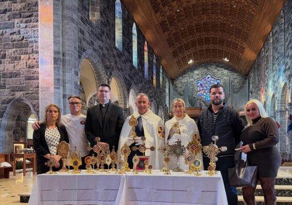 A group of people stand behind a table displaying several golden reliquaries inside a stone church.