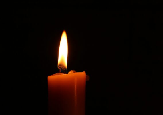 A lit candle with a bright flame against a black background.